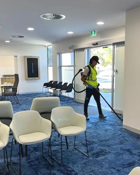 A Living Fresh cleaner in hi-vis vacuuming the waiting room of a Perth clinic
