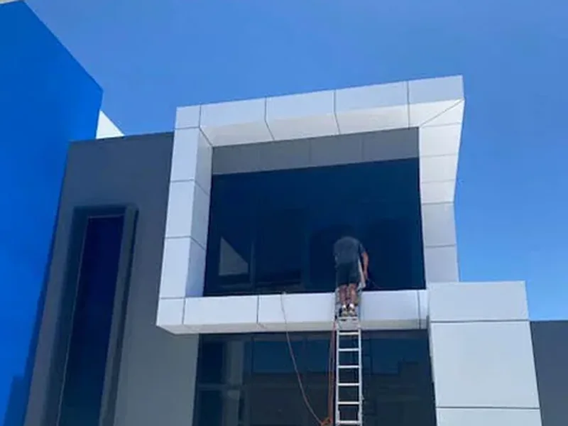 A cleaner on a ladder washing the glazing of a newly built commercial unit